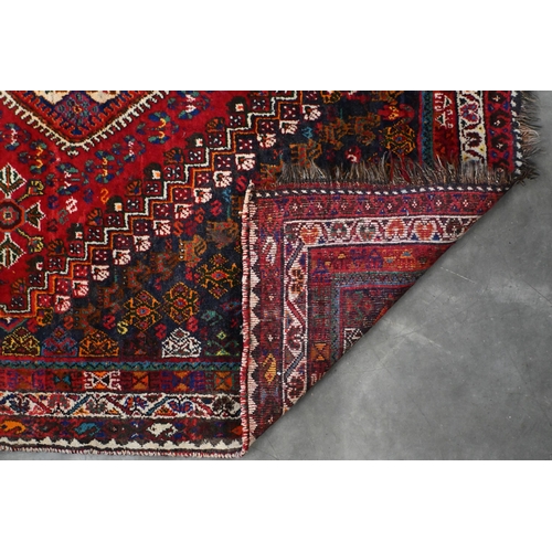 203 - A vintage Persian shiraz rug with triple lozenge medallion with floral and fauna design on red groun... 