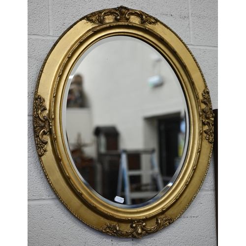 164 - A bevelled oval wall mirror in ornate gilt wood and gesso frame, 66 cm h x 55 cm w