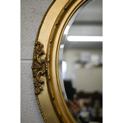 164 - A bevelled oval wall mirror in ornate gilt wood and gesso frame, 66 cm h x 55 cm w