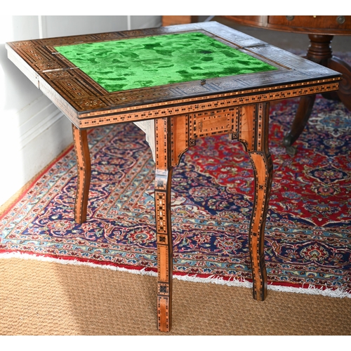 A vintage Damascus games table, 20th century, Syria, profusely parquetry inlaid with specimen timbers and mother-of-pearl overall, the fold over top with green fabric surface, back gammon and chess boards, raised on conforming shaped legs