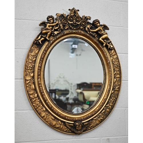 223 - A modern oval wall mirror in decorative gilt frame with foliate designs surmounted by cherubs, 98 cm... 