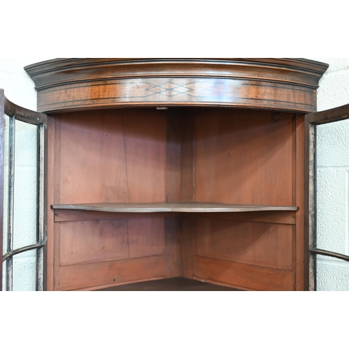 71 - An Edwardian mahogany barrel-front corner cabinet with glazed doors enclosing shelves on cabinet bas... 