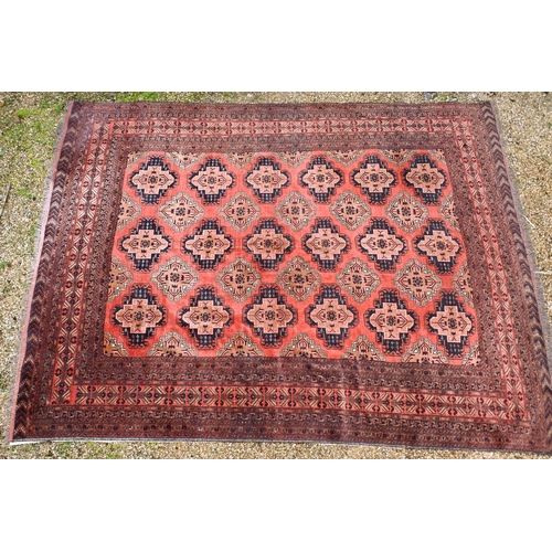630 - An old Afghan Turkman design carpet, the orange-red ground with four rows of geometric guls, 395 cm ... 