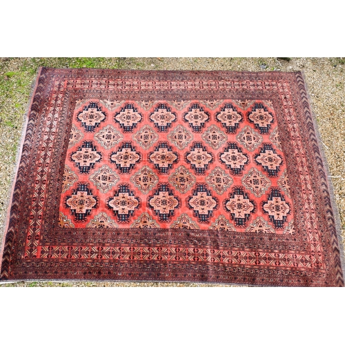 630 - An old Afghan Turkman design carpet, the orange-red ground with four rows of geometric guls, 395 cm ... 