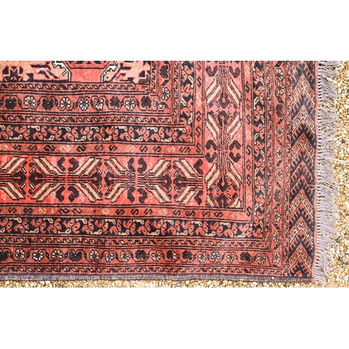 630 - An old Afghan Turkman design carpet, the orange-red ground with four rows of geometric guls, 395 cm ... 