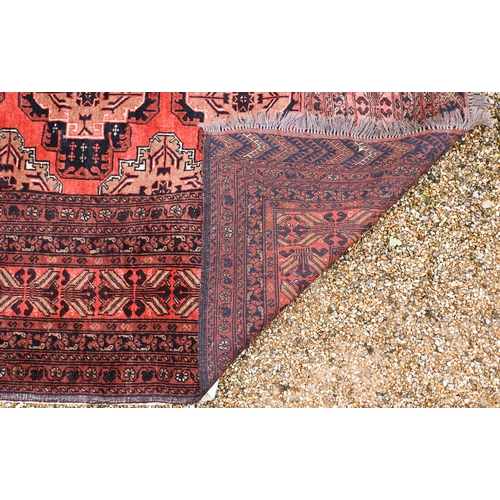 630 - An old Afghan Turkman design carpet, the orange-red ground with four rows of geometric guls, 395 cm ... 