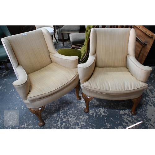 125 - A pair of Georgian style wingback armchairs, with shaped arms and bowfront seats, raised on walnut s...