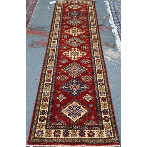 595 - A Persian Kazhak runner with geometric medallions on red ground with blue and beige borders, 282 x 8... 