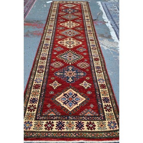 595 - A Persian Kazhak runner with geometric medallions on red ground with blue and beige borders, 282 x 8... 