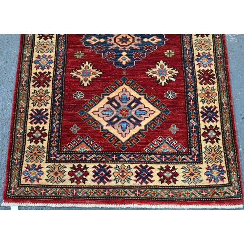 595 - A Persian Kazhak runner with geometric medallions on red ground with blue and beige borders, 282 x 8... 