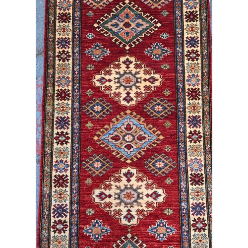595 - A Persian Kazhak runner with geometric medallions on red ground with blue and beige borders, 282 x 8... 
