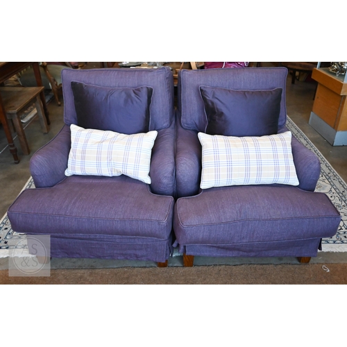 A pair of country house Howard style armchairs with deep seats and low rolled arms in loose purple fabric covers, square hardwood supports (back legs with castors), each with purple and plaid cushions, 88 x 100 x 82 cm high