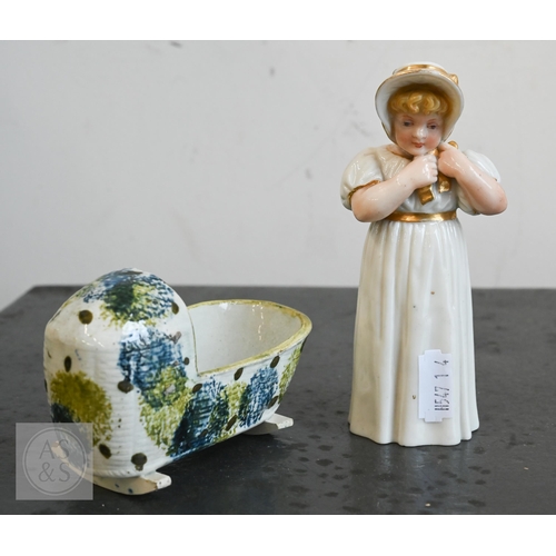 A Georgian Pratt-type pearlware doll's house cradle with incised basket work and sponged decoration, 10 cm long, to/w a Victorian Royal Worcester figural candle snuffer as a young girl tying her bonnet, circa 1880 (2)