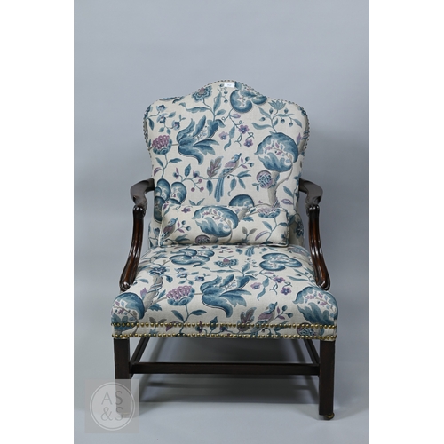 A Georgian carved mahogany framed Gainsborough library chair, the serpentine crest overstuffed back, arms and seat with brass studs, raised on square front legs united by an H-stretcher, on brass rollers, the leaf pattern upholstery later