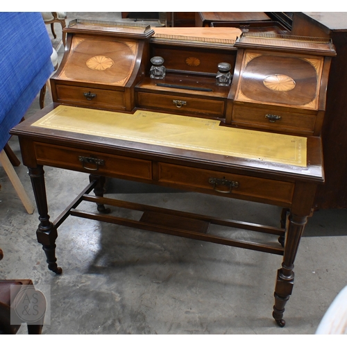 An Edwardian walnut Carlton house desk, the raised back with pierced brass gallery and stationery compartments with satin patera inlay either side of the central drawer and two glass inkwells over a tooled leather top and two frieze drawers raised on turned fluted supports and casters, 106 x 54 x 100 cm high
