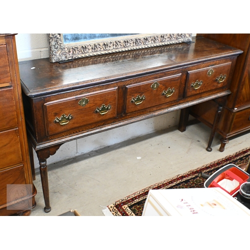 213 - A George III oak low dresser, three drawers with traditional brass handles raised on turned supports...