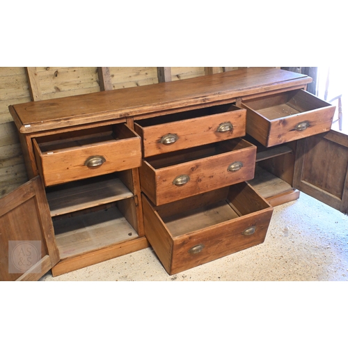 42 - An old stained pine low dresser centred by three short drawers flanked by a drawer over cupboard to ... 