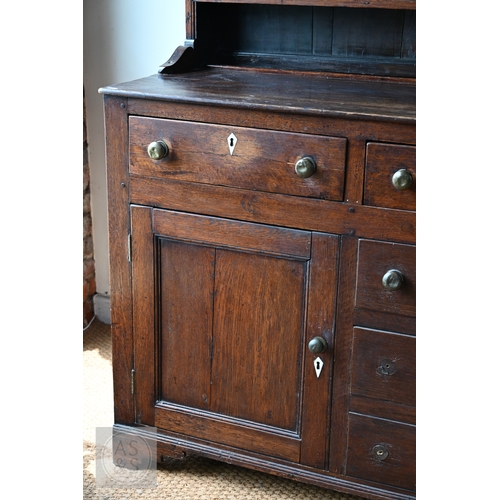 604 - An 18th century oak high dresser, the plank back open three tier rack over a base centred by four dr... 