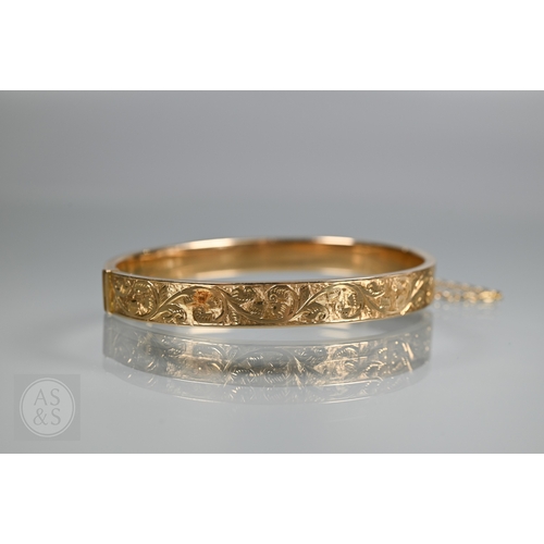 254 - A yellow metal oval hinged bangle with part foliate engraved decoration, stamped 15ct, concealed cla... 
