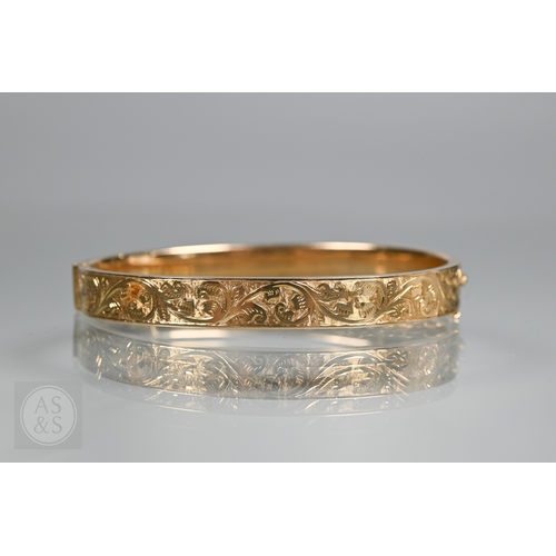 254 - A yellow metal oval hinged bangle with part foliate engraved decoration, stamped 15ct, concealed cla... 