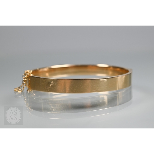 254 - A yellow metal oval hinged bangle with part foliate engraved decoration, stamped 15ct, concealed cla... 