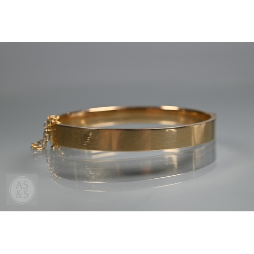 254 - A yellow metal oval hinged bangle with part foliate engraved decoration, stamped 15ct, concealed cla... 