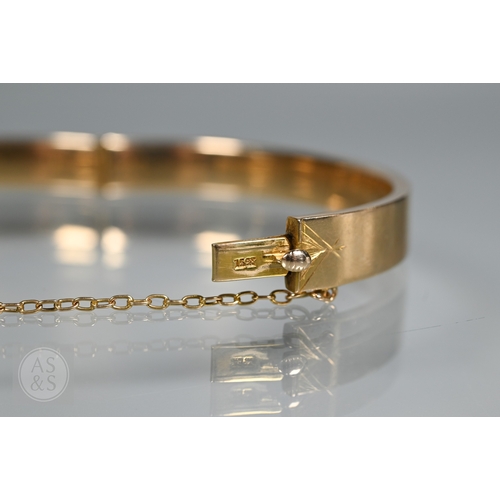 254 - A yellow metal oval hinged bangle with part foliate engraved decoration, stamped 15ct, concealed cla... 