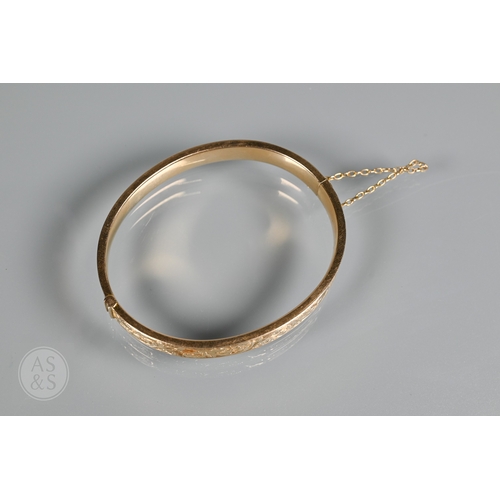 254 - A yellow metal oval hinged bangle with part foliate engraved decoration, stamped 15ct, concealed cla... 