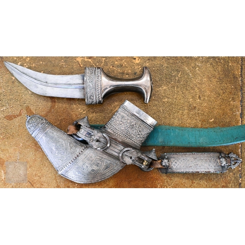 An antique Omani silver-mounted dagger Jambiya with ribbed and curved 16.5cm blade on foliate-engraved and horn hilt, the scabbard with conforming decoration and woven silver wire, on similarly-decorated belt