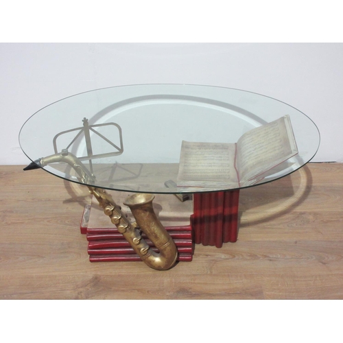 108 - A modern oval glass topped Coffee Table with a music themed base 3ft 9in W x 1ft 7in H