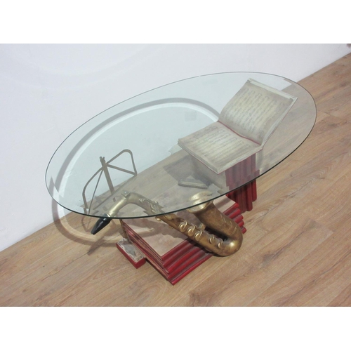 108 - A modern oval glass topped Coffee Table with a music themed base 3ft 9in W x 1ft 7in H