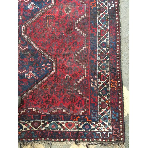 18 - An Oriental woollen red ground Rug with central row of three interlocking lozenges within cream and ... 