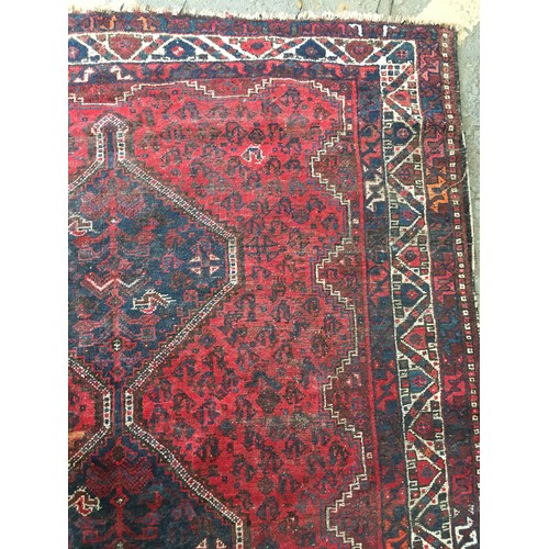 18 - An Oriental woollen red ground Rug with central row of three interlocking lozenges within cream and ... 