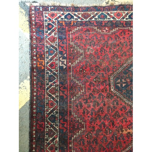 18 - An Oriental woollen red ground Rug with central row of three interlocking lozenges within cream and ... 