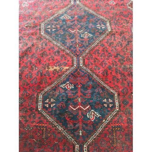 18 - An Oriental woollen red ground Rug with central row of three interlocking lozenges within cream and ... 