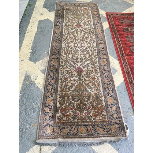 28 - A beige ground Runner decorated with Tree of Life, approx 9ft 10in L x 3ft 2in W and a modern red gr... 