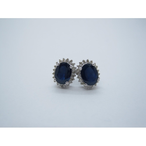 125 - A pair of Sapphire and Diamond Cluster Earrings, each claw-set oval-cut sapphire within frame of bri... 