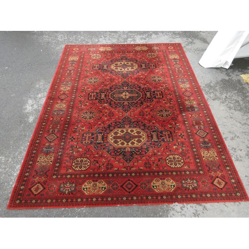 453 - A large red ground Rug with multi-geometric design borders, with three large central floral/geometri... 