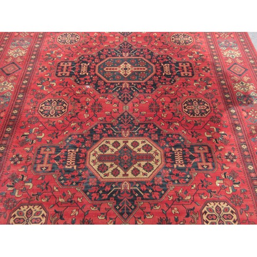 453 - A large red ground Rug with multi-geometric design borders, with three large central floral/geometri... 