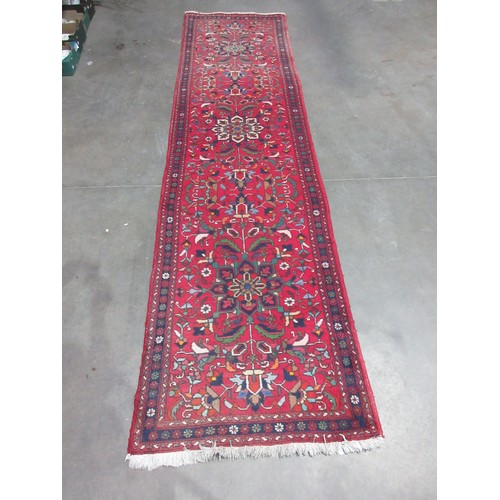 551 - An Iranian red ground woollen Runner with three stylised floral motifs amongst further stylised flow... 