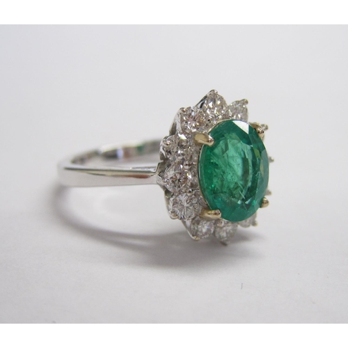 202 - An Emerald and Diamond and Cluster Ring claw-set oval-cut emerald, 1.75cts, within  frame of twelve ... 