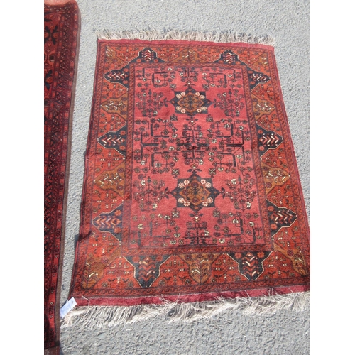 65 - A red ground Rug with blue stylised leafage design 6ft 6in L x 4ft 4in W and another smaller red gro... 