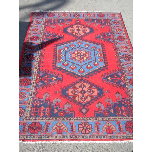 66 - A red ground Rug with blue central hexagonal motif 7ft L x 5ft 4in W