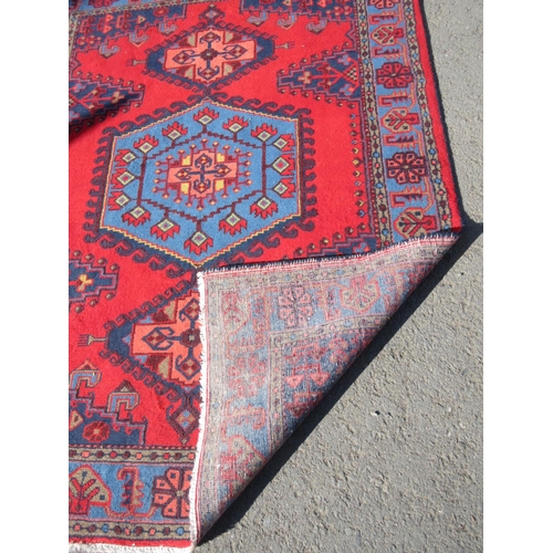 66 - A red ground Rug with blue central hexagonal motif 7ft L x 5ft 4in W