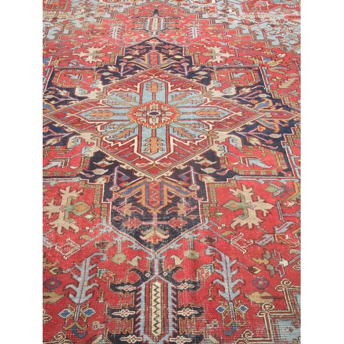 70 - A large red ground Rug with central floral motif within blue border 13ft 4in L x 9ft 10in W