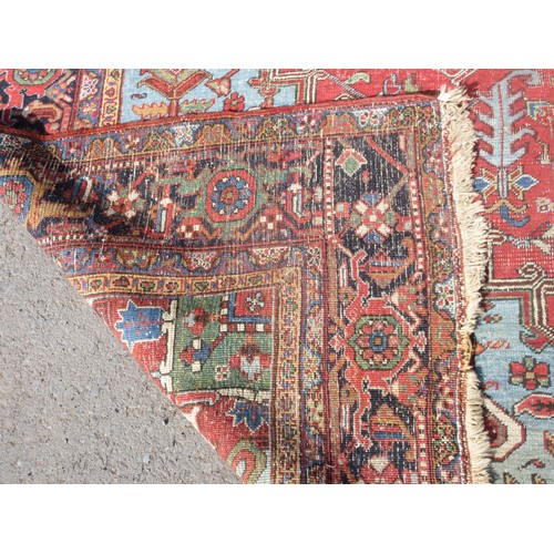 70 - A large red ground Rug with central floral motif within blue border 13ft 4in L x 9ft 10in W