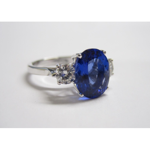 171 - A Tanzanite and Diamond three stone Ring claw-set oval-cut tanzanite, 3.38cts, between two brilliant... 