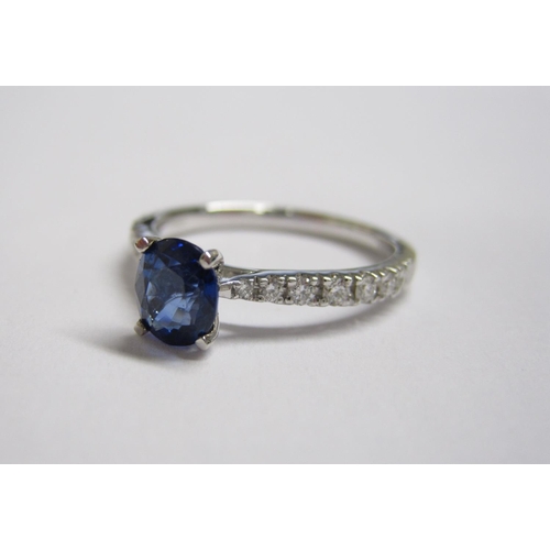 184 - A Sapphire and Diamond Ring claw-set oval-cut sapphire between graduated brilliant-cut diamonds pave... 