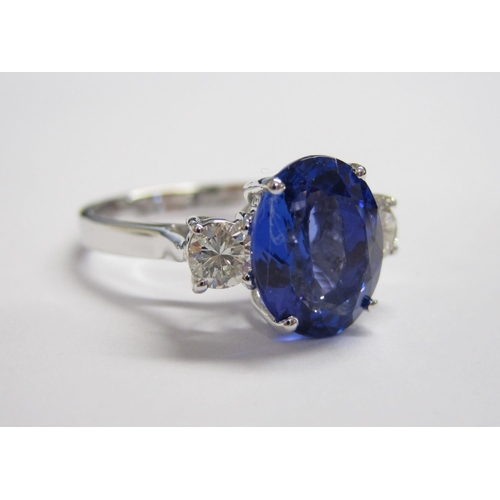 173 - A Tanzanite and Diamond three stone Ring claw-set oval mixed-cut tanzanite, 3.30cts, between two bri... 