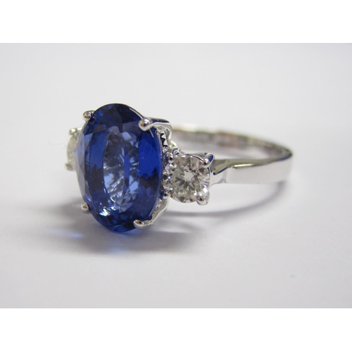 173 - A Tanzanite and Diamond three stone Ring claw-set oval mixed-cut tanzanite, 3.30cts, between two bri... 